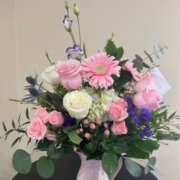 Pink and white mixed flower arrangement with purple accents in a pink ceramic pitcher.