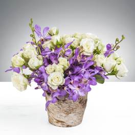 Compact arrangement of white roses and purple orchids in a rustic birch pot