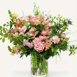 Tall pink mixed flower arrangement with roses, orchids, and snapdragons in a clear glass cylinder vase