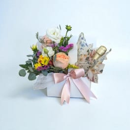 Mixed flower arrangement in a white box with a pink ribbon