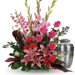 Pink and red funeral bouquet beside a silver urn