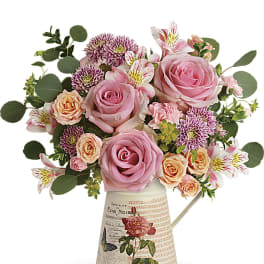 Pink roses and mixed blooms arranged in a decorative pitcher vase
