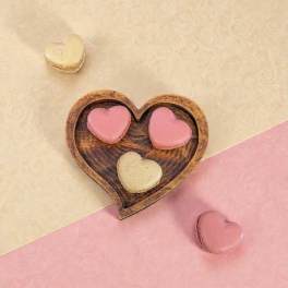 Heart-shaped macarons in a wooden heart dish on pink and cream paper