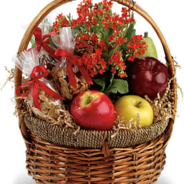 Gift basket with flowers, apples, and wrapped snacks in a wicker basket