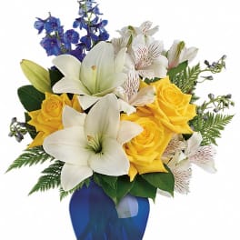 Bouquet of yellow roses, white lilies, and blue flowers in a cobalt vase