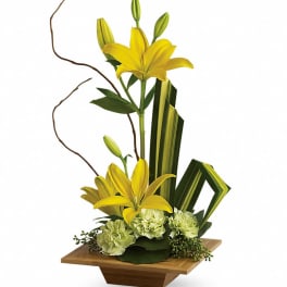 Yellow lilies in a wooden vase with green carnations and decorative leaves