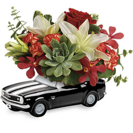 Flower arrangement in a black toy car container with red and white blooms