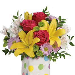 Bouquet of pink roses, yellow lilies, and daisies in a polka-dot vase