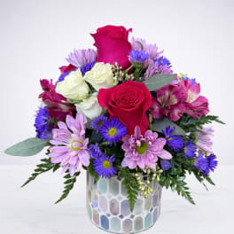 Mixed arrangement of hot pink roses, white roses and purple daisies in an iridescent mosaic vase