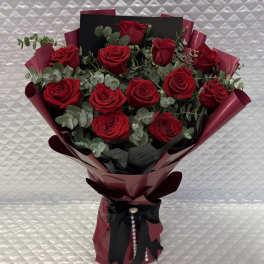 Bouquet of red roses wrapped in burgundy paper with a black ribbon