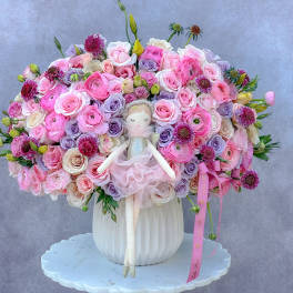 Large pink and lavender rose arrangement with a doll in a white vase