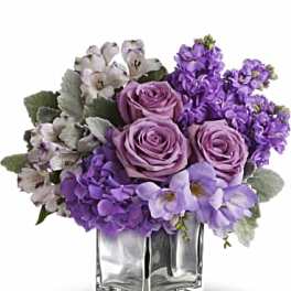 Purple roses and mixed lavender flowers in a clear square vase