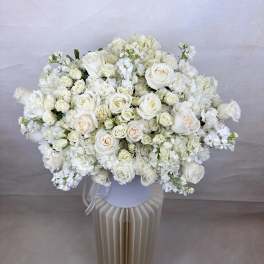 Large all-white bouquet of roses and hydrangeas in a white hatbox vase on a pedestal