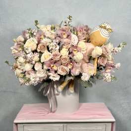 Large pastel pink and cream flower arrangement in a white hatbox with a plush ballerina doll nestled among the blooms