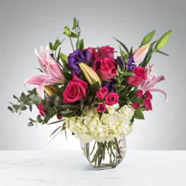 Bouquet of pink roses, lilies, and purple blooms in a glass vase