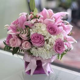 Pink lilies and roses arranged in a purple box with a ribbon