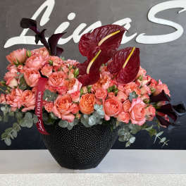 Pink and coral roses in a black vase with dark red anthuriums