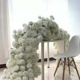 White floral arch draped over a table beside a white chair