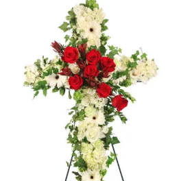 Standing cross-shaped spray of white flowers with red roses and trailing ivy on an easel.