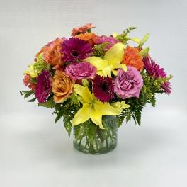 Bright mixed bouquet of yellow lilies, pink gerbera daisies, and roses in a clear glass vase