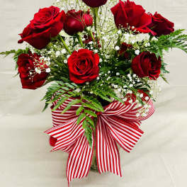 Red roses arranged in a vase with baby's breath and a striped ribbon