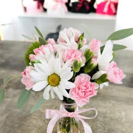 Pink carnations and white daisies in a clear glass vase with a pink ribbon
