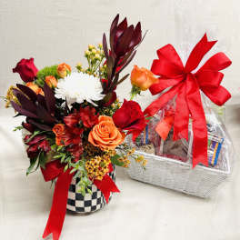 Mixed flower arrangement in a checkered vase beside a wrapped gift basket
