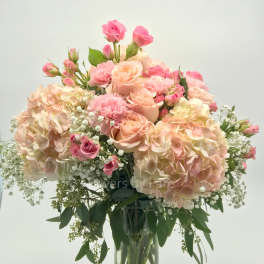 Tall glass vase arrangement of blush hydrangeas, pink roses, carnations, and baby's breath.