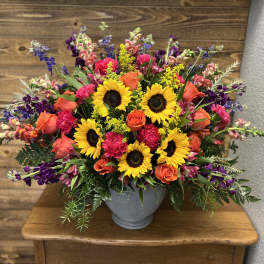 Mixed bouquet with sunflowers, orange roses, and purple flowers in a gray vase