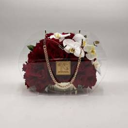 Red roses and white orchids in a clear round handbag-style container