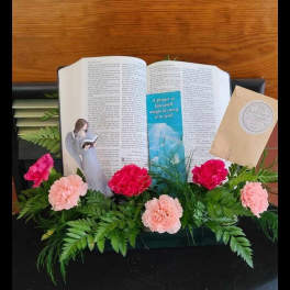Pink carnations arranged around an open Bible with an angel figurine