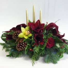 Low floral centerpiece with red blooms, pinecones, and gold candles