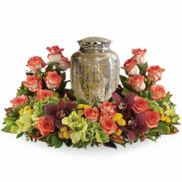 Coral roses and orchids arranged around an ornate silver urn