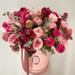 Pink and burgundy flower arrangement in a round hatbox with ribbon