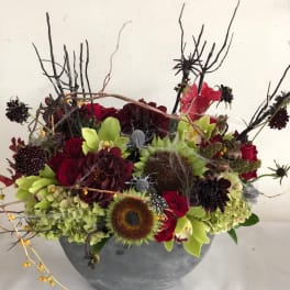 Mixed floral arrangement in a gray bowl with dark branches and red blooms