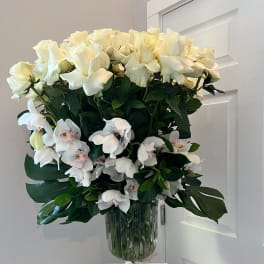 White roses and orchids arranged in a glass vase with a ribbon.
