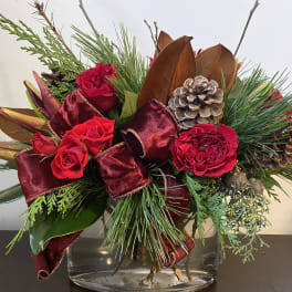 Red roses in a glass vase with burgundy ribbon and pinecones