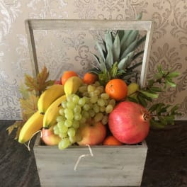 Wooden crate filled with assorted fruit including bananas, grapes, oranges, and pomegranates