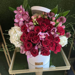 Round white hat box filled with red roses, pink orchids, and white blooms on a gold stand
