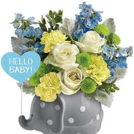 Blue and yellow flower arrangement in a gray elephant vase with a baby sign