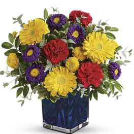 Mixed bouquet of yellow, purple, and red flowers in a blue glass vase