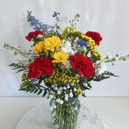 Mixed bouquet of red, yellow, white, and blue flowers in a glass vase