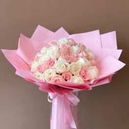 Bouquet of pink and white roses wrapped in pink paper in a glass vase