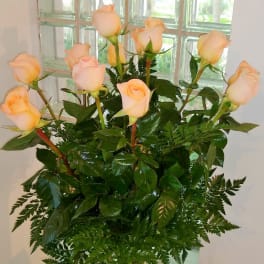Peach roses arranged in a clear glass vase with fern foliage