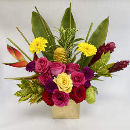 Tropical arrangement with bright roses and gerbera in a gold cube vase