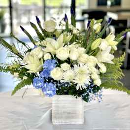 White and blue flower arrangement with roses, lilies, and mums in a white wooden box on a table