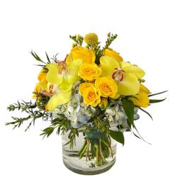 Yellow roses and orchids arranged in a glass vase