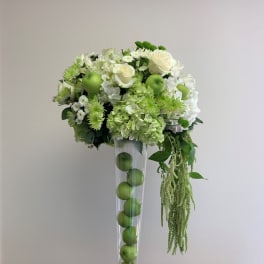 White and green floral arrangement in a tall clear vase with apples inside