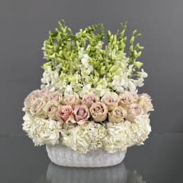 White and blush roses with white orchids in a white ceramic vase