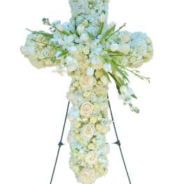 White floral cross on a stand with roses and hydrangeas
